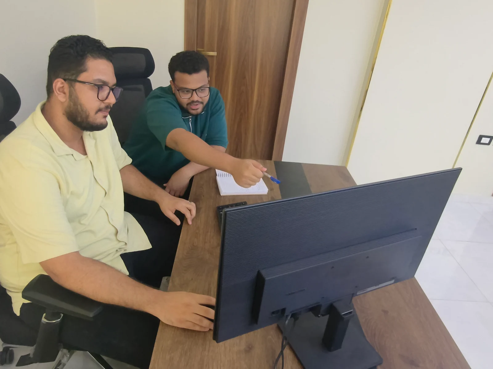 أحمد سعد وأحمد علي يناقشان العمل أمام شاشة في المكتب